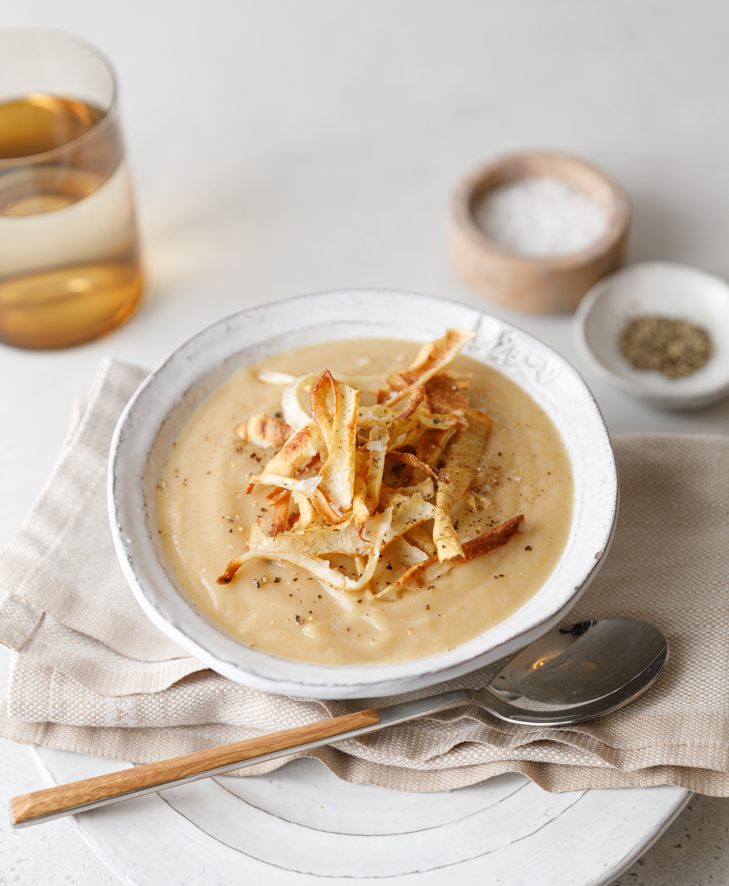 45 degree image of Parsnip & Ginger Soup with a glass of water and salt and pepper pinch pots