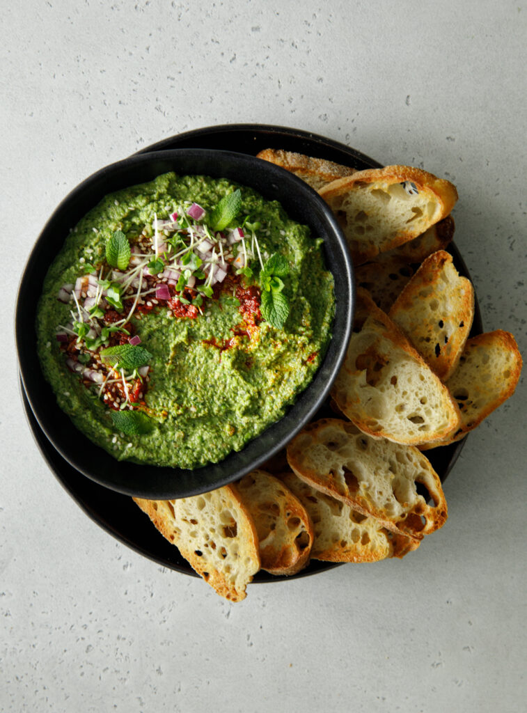 Green pea, lentil and mint dip in a black bowl with toasted ciabatta slices