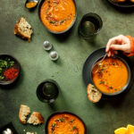 2 bowls Spiced sweet potato and orange soup on a green textured backdrop