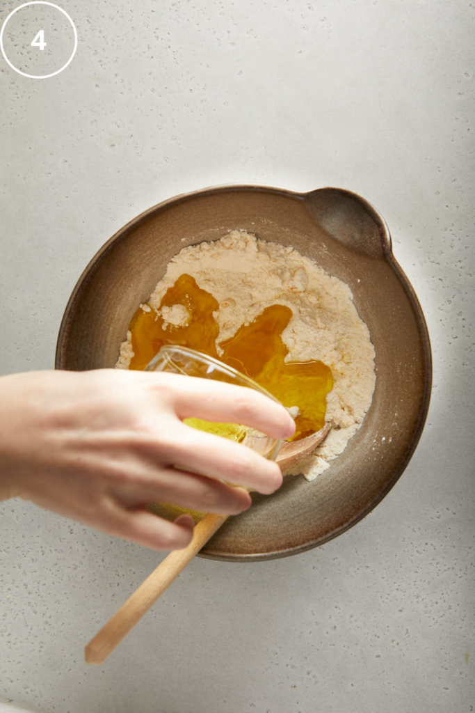 olive oil being poured into the mixing bowl with dry ingredients in 