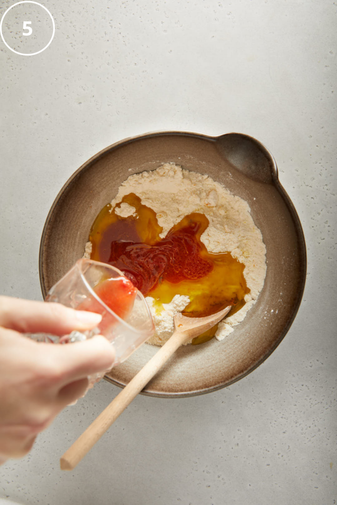 blood orange juice being poured into the mixing bowl with dry ingredients in 