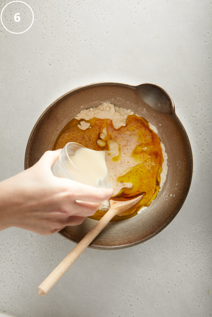soy milk being poured into the mixing bowl with dry ingredients in 