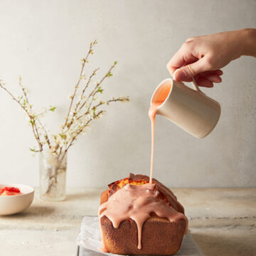 Image of finished blood orange loaf with the blood orange sugar drizzle being poured on out of a jug