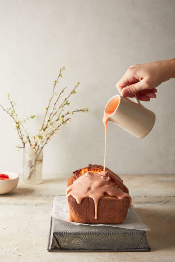 Image of finished blood orange loaf with the blood orange sugar drizzle being poured on out of a jug