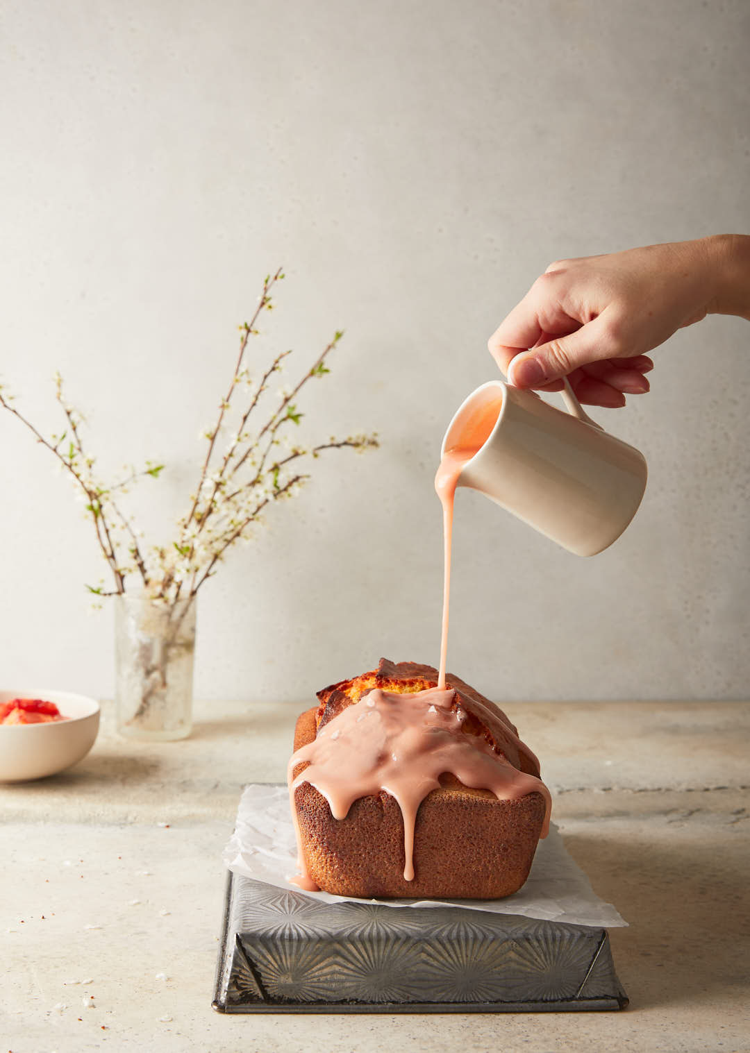 Image of finished blood orange loaf with the blood orange sugar drizzle being poured on out of a jug 