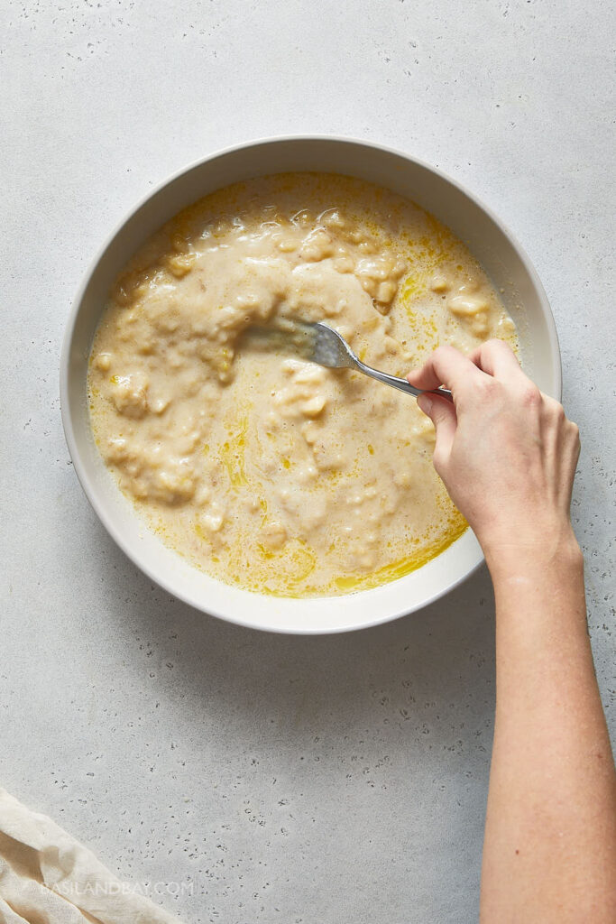 banana and wet ingredients being stirred in the large beige mixing bowl
