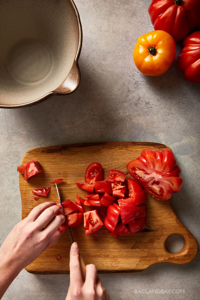 heritage tomato being diced into large chunks on a wooden chopping board