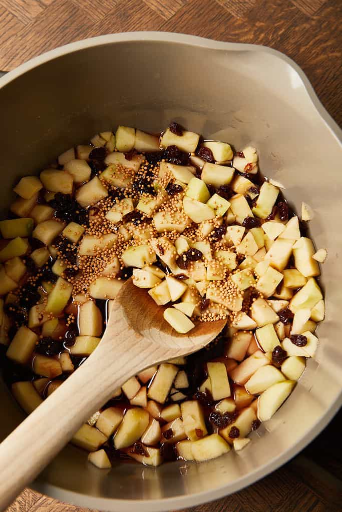 Image of chopped apples, raisins  and mustard seeds mixture in a large saucepan