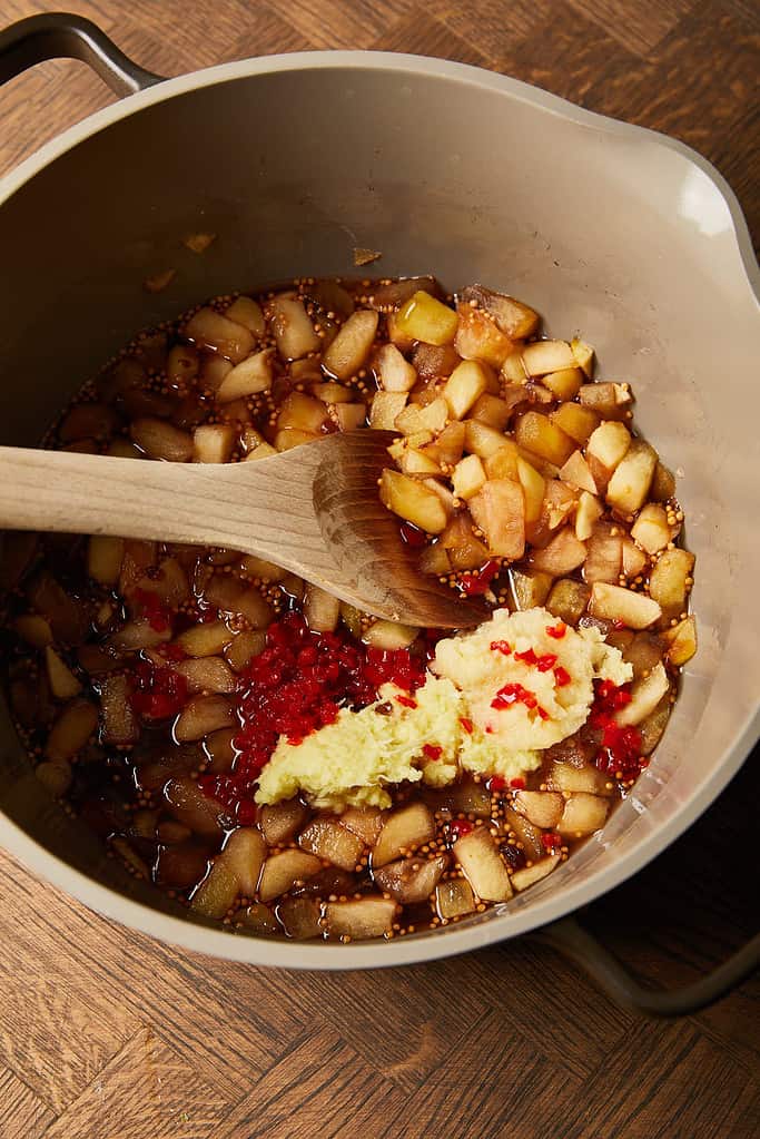 Image of minced garlic, ginger and chilli being added to cooked apples and raisins  mixture in a large saucepan 