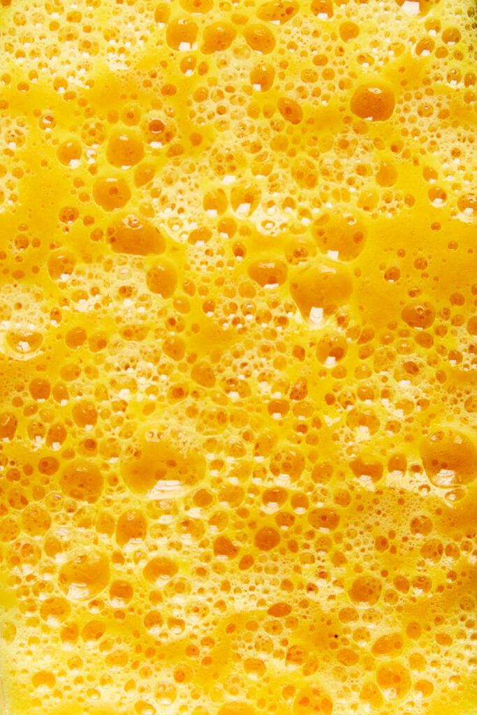 macro close up shot of the bubbles of Orange pineapple and ginger immunity juice in a vitamix blender jug
