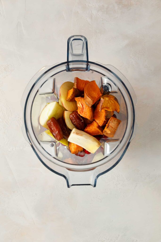 Fresh Ginger and sliced apples and cooked sweet potato chunks layered on top of frozen grapes and cranberries in a blender jug.