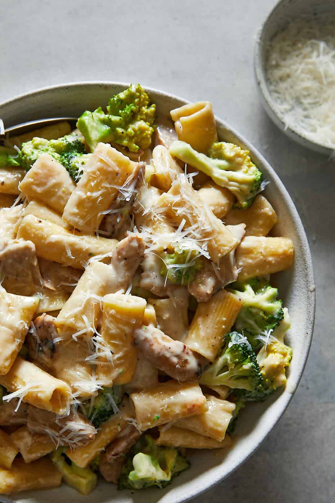 Vegan Chicken & Broccoli Alfredo on a grey backdrop with a small bowl of parmesan and a white striped linen