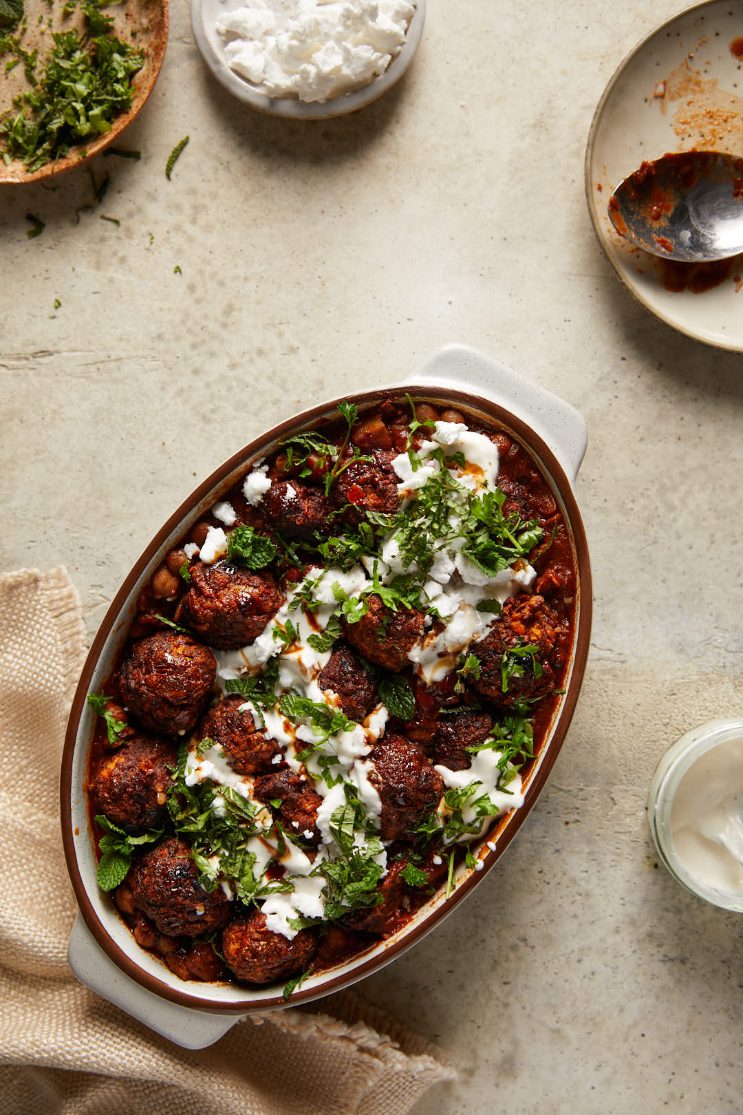 flat lay image of Spicy harissa vegan meatballs in a oval casserole dish on a grey stone backdrop