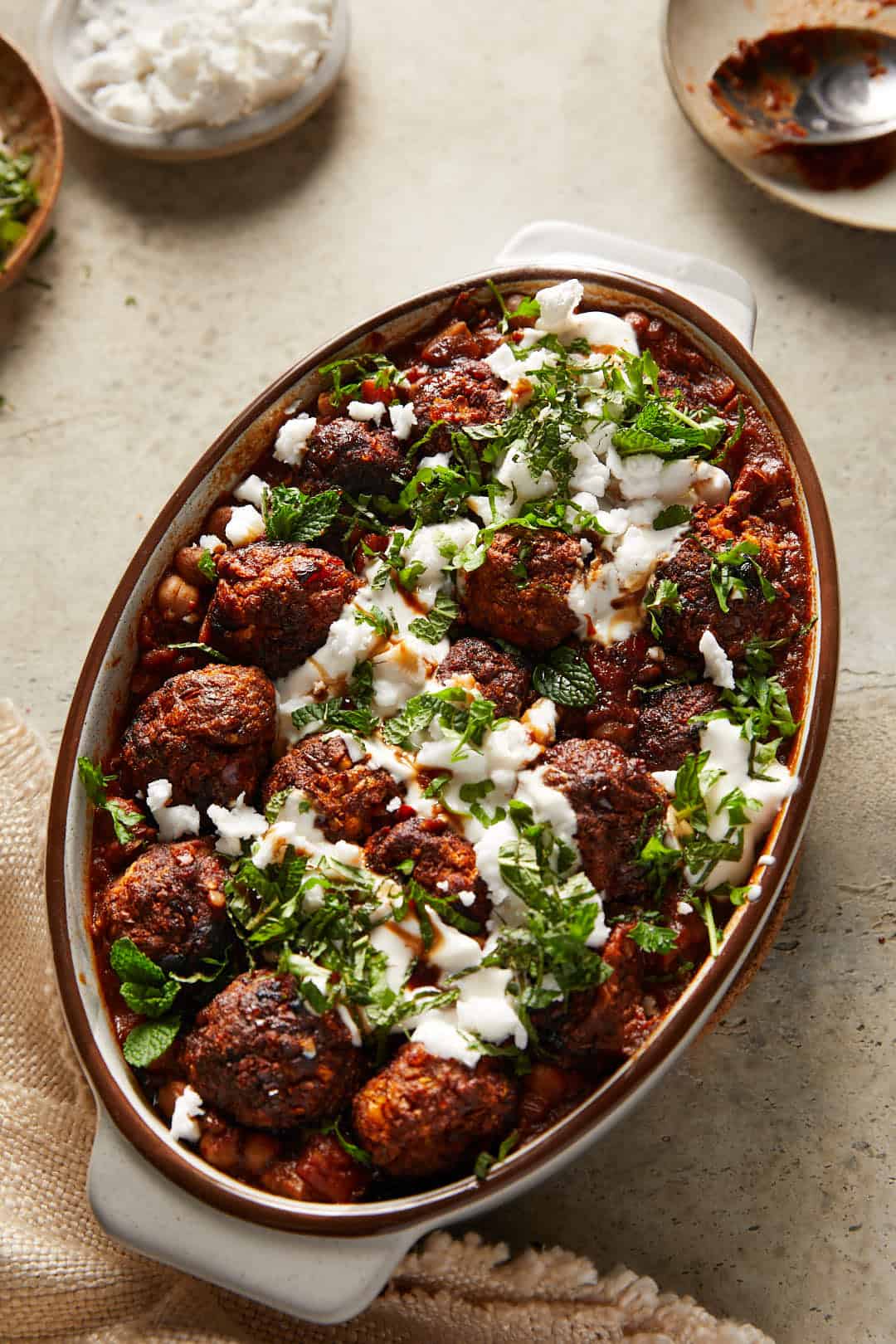 Spicy harissa vegan meatballs in a oval casserole dish on a grey stone backdrop