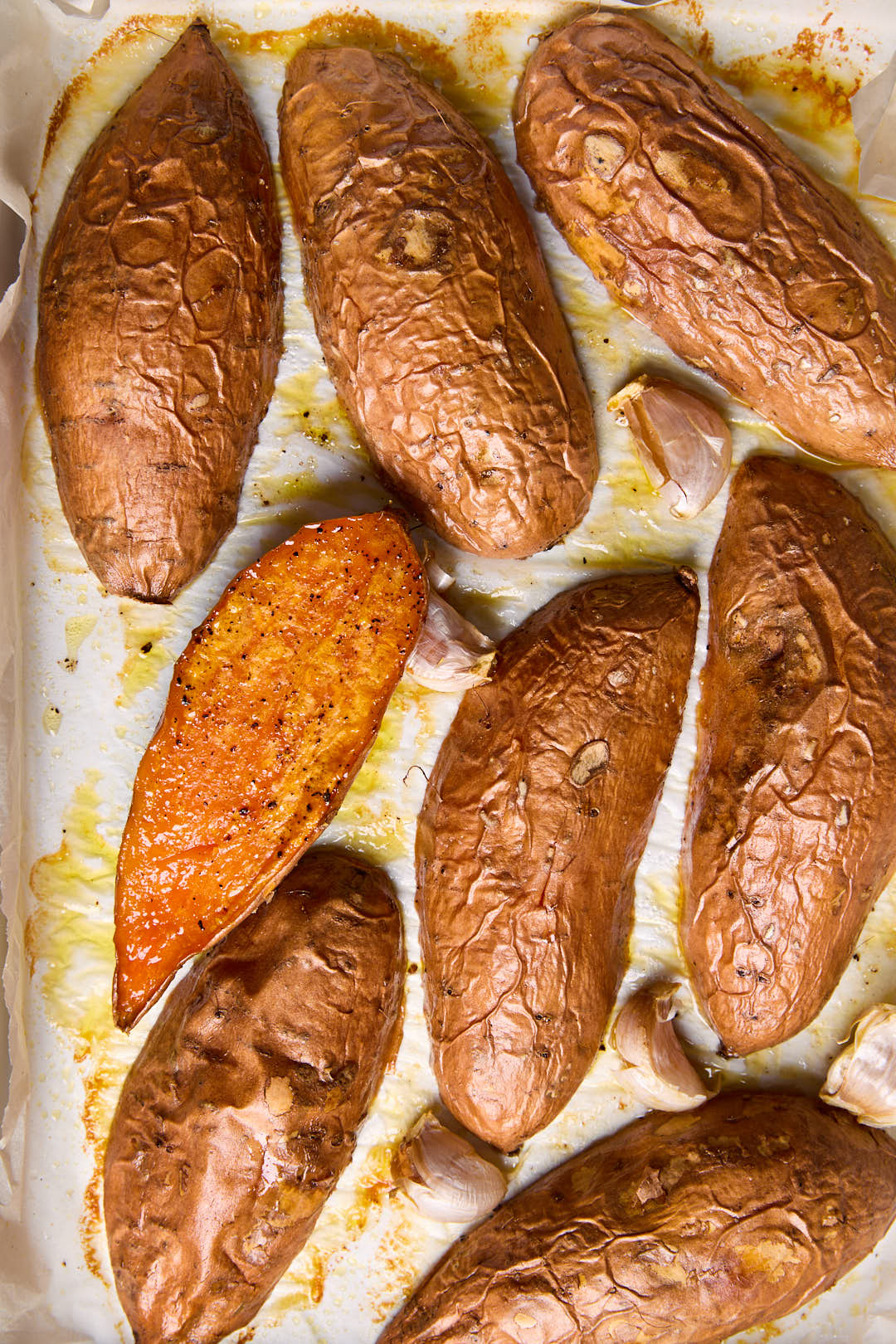 Roasted sweet potatoes on a baking sheet, all face down apart from one to show the cooked texture