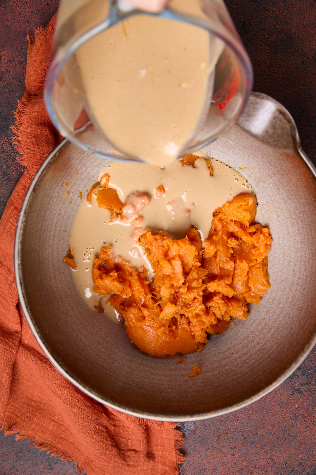 Miso, tahini and stock mixture being added to the mixture of sweet potato mash