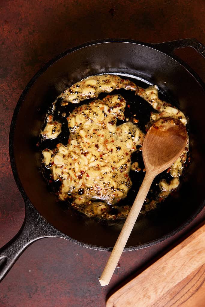 garlic and red pepper flakes in a cast iron pan being sautéed in vegan butter 