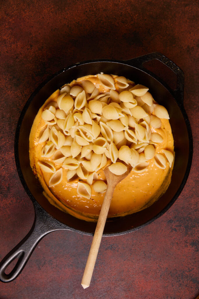 pasta shells being added to the pumpkin pasta sauce in a cast iron pan