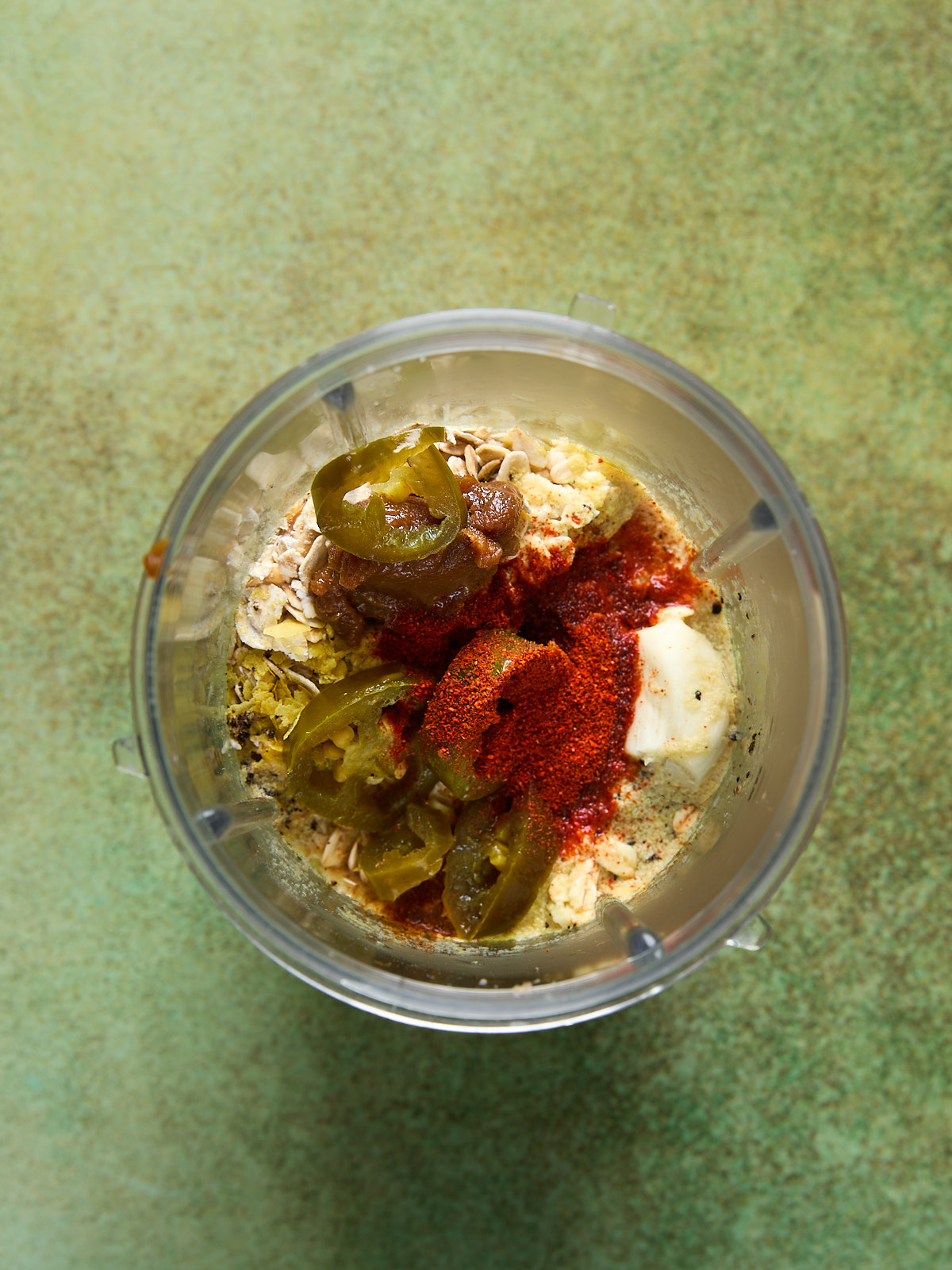 Blender cup with jalapeños, chili powder, and smoked paprika added on top of the base ingredients