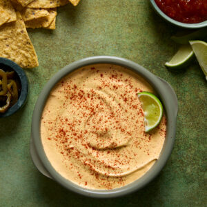 Nacho Queso Dip on a green backdrop with accompaniments