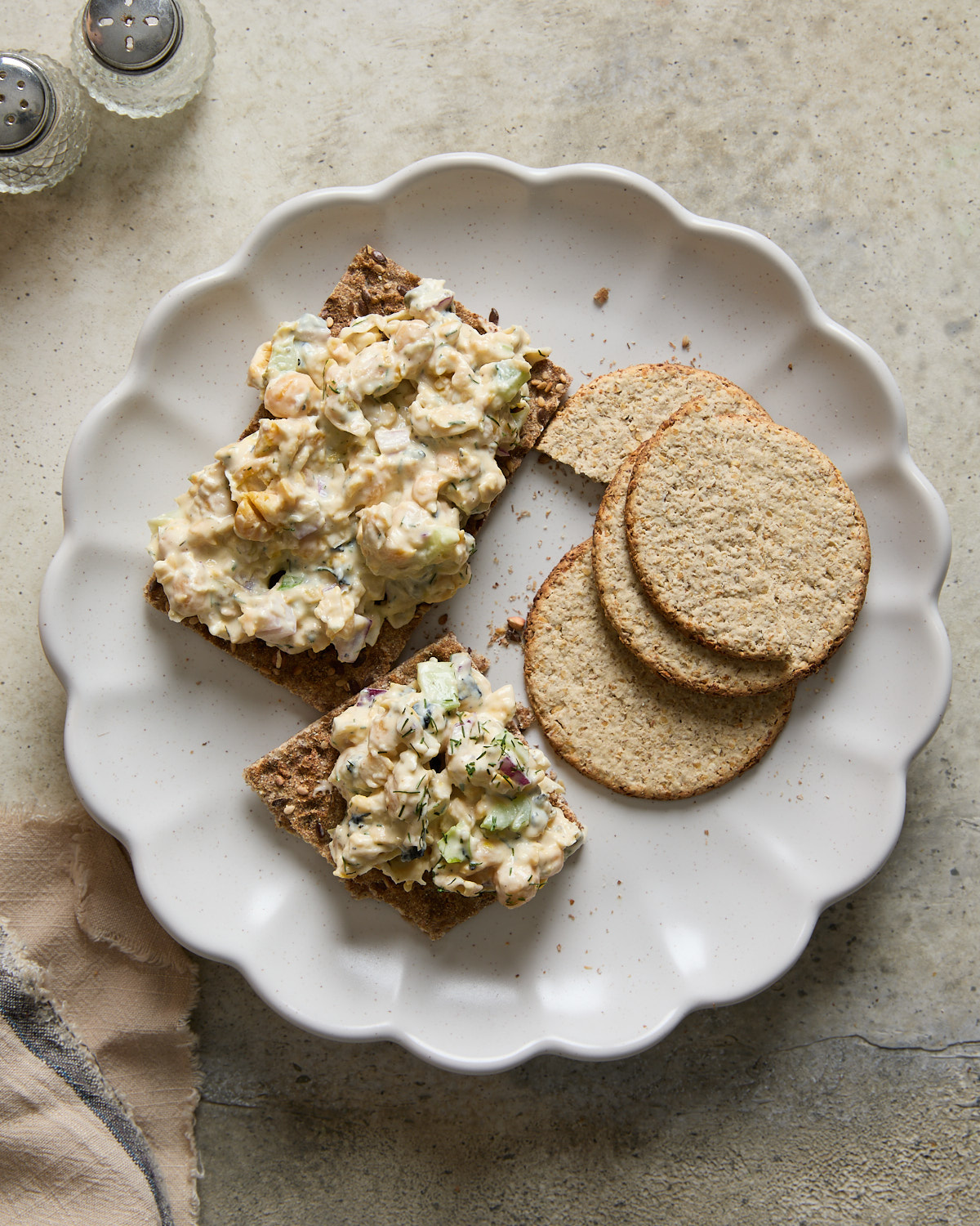 Vegan chickpea tuna salad served on crispbread with oat crackers on a scalloped plate