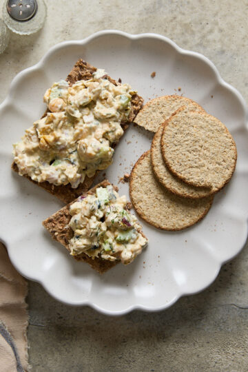 Vegan chickpea tuna salad served on crispbread with oat crackers on a scalloped plate