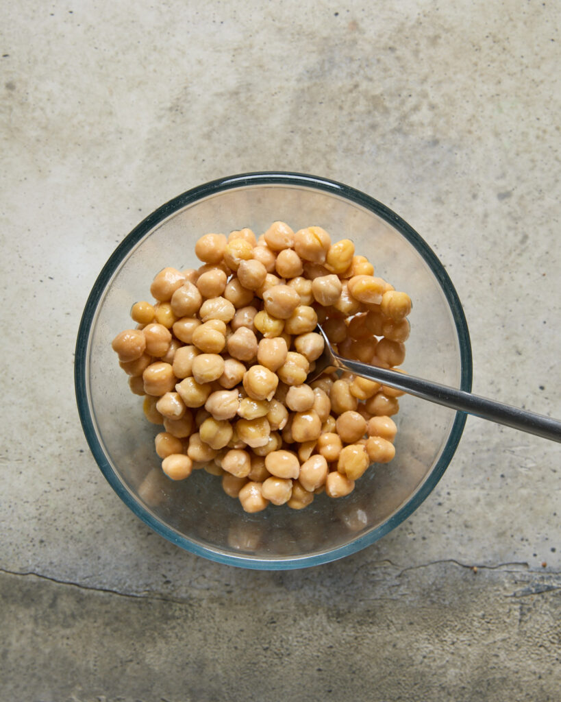 Glass bowl of chickpeas tossed in olive oil and sea salt before cooking.