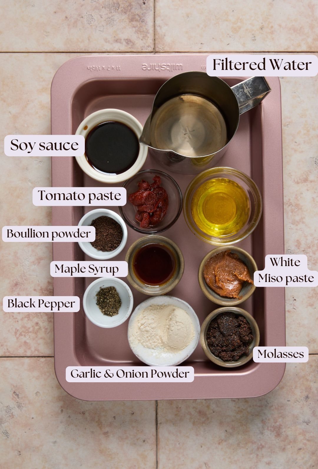 A tray holds labeled bowls of ingredients: soy sauce, tomato paste, bouillon powder, maple syrup, black pepper, garlic & onion powder, filtered water, olive oil, white miso paste, and molasses.