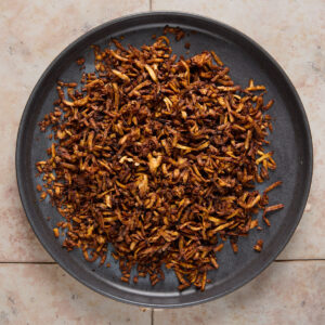 A dark plate filled with a heap of crispy, browned fried onions sits on a light-colored tiled surface.