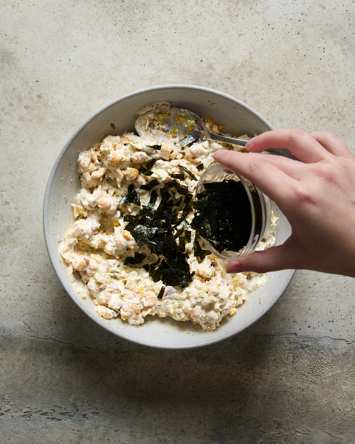 Hand adding chopped nori to a bowl of vegan chickpea tuna salad mixture