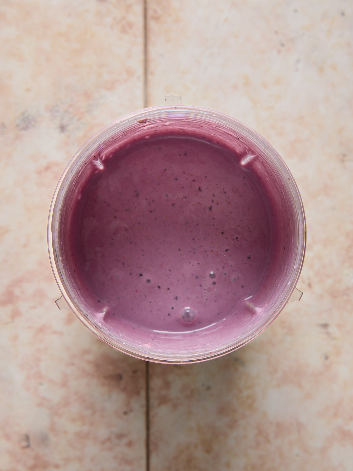 Top-down view of a thick, creamy berry smoothie freshly blended in a blender cup with a vibrant purple color.
