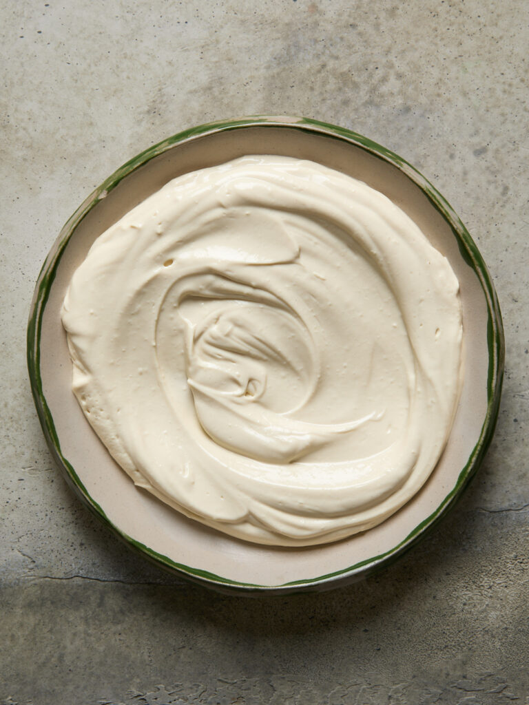A smooth, creamy swirl of whipped tofu ricotta in a shallow dish, with a silky texture and pale, light colour.

