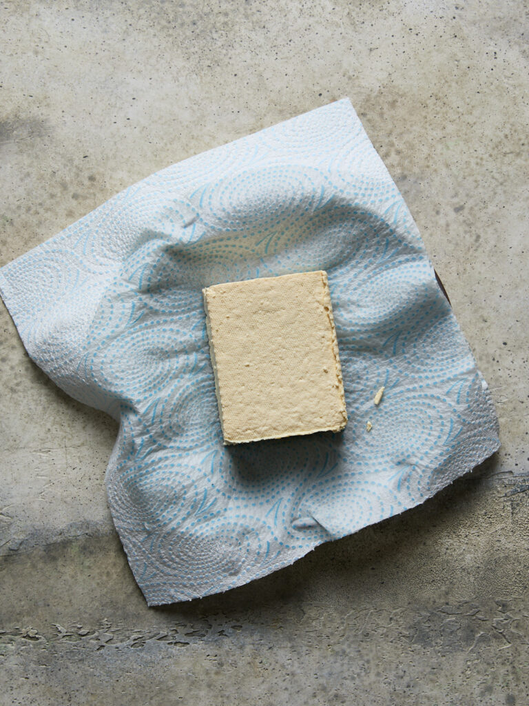 A block of firm tofu resting on paper towel to drain excess moisture before blending for ricotta.