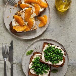 Two plates of toast-one with sweet ricotta and orange, the other with savoury ricotta and fresh green peas, mint, and cracked pepper.