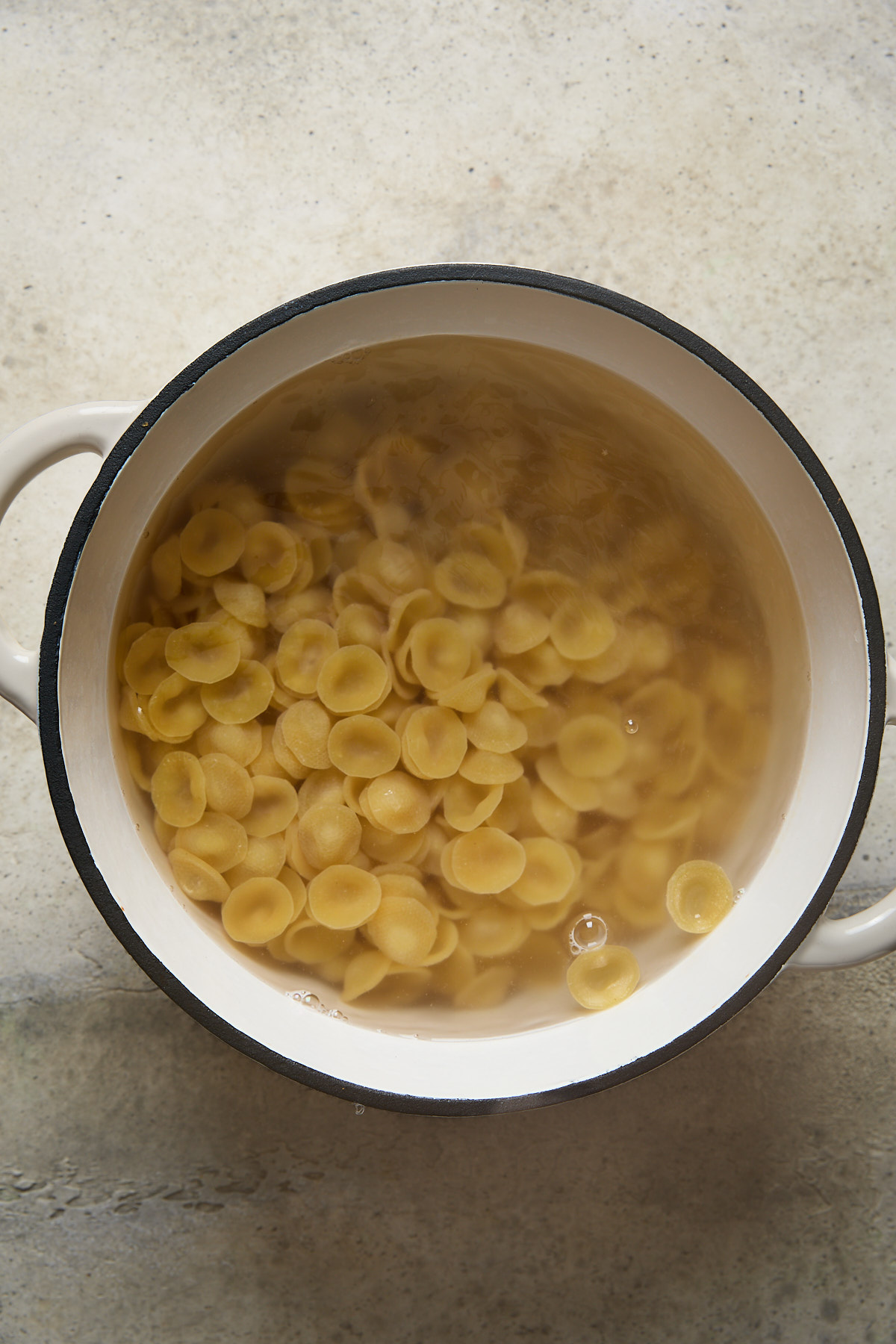 Orecchiette pasta boiling in a white pot of salted water, just beginning to soften.