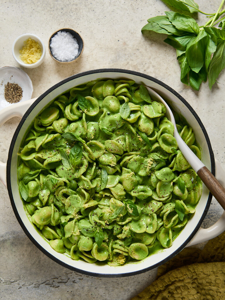 Large pot filled with orecchiette coated in silky green sauce, topped with basil, lemon zest, and cracked pepper, ready to serve.