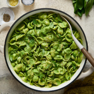 Large pot filled with orecchiette coated in silky green sauce, topped with basil, lemon zest, and cracked pepper, ready to serve.