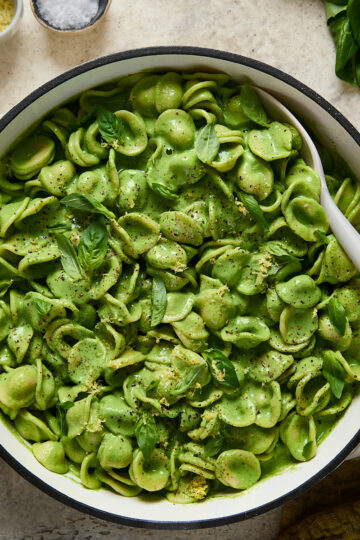 Large pot filled with orecchiette coated in silky green sauce, topped with basil, lemon zest, and cracked pepper, ready to serve.