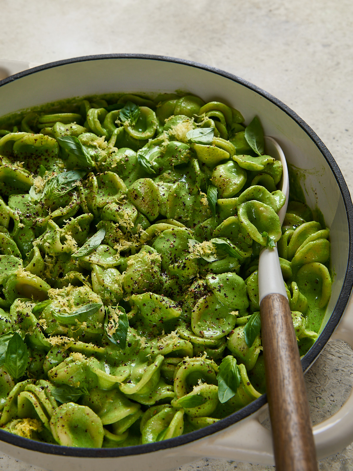 Large pot filled with orecchiette coated in silky green sauce, topped with basil, lemon zest, and cracked pepper, ready to serve.