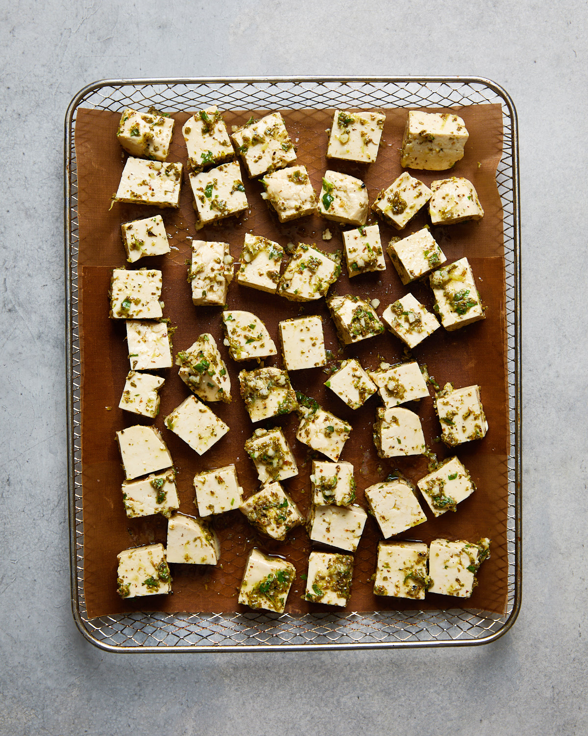 Uncooked marinated tofu cubes spread out on a parchment-lined air fryer tray, ready to be baked or air-fried.