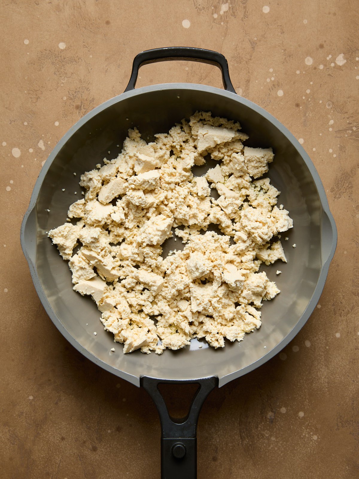 Crumbled firm tofu in a large non-stick frying pan, ready to be cooked for the base of the scramble.
