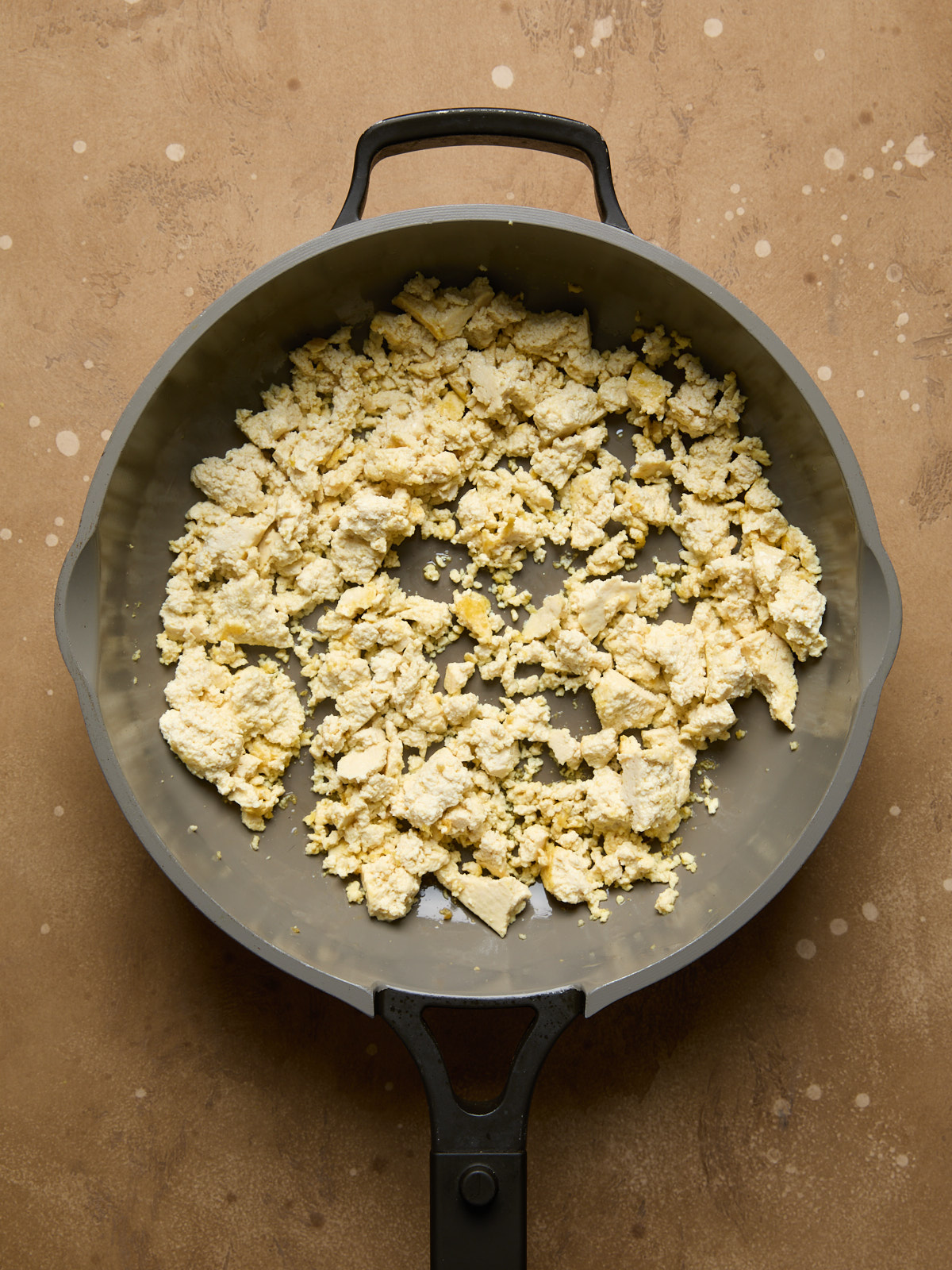 Tofu starting to turn golden after pan-frying for a few minutes, breaking into smaller, soft chunks.